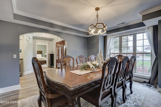 dining space featuring crown molding, a chandelier, a textured ceiling, and light hardwood / wood-style floors