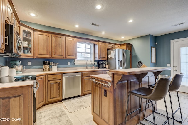 kitchen with sink, a kitchen island, stainless steel appliances, a textured ceiling, and a kitchen bar