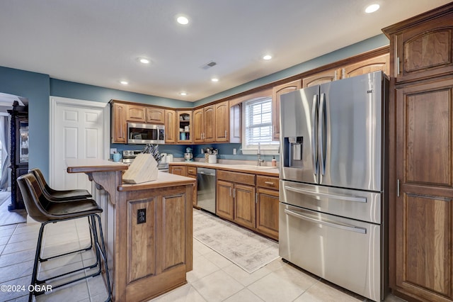 kitchen with sink, a breakfast bar, appliances with stainless steel finishes, a center island, and light tile patterned flooring