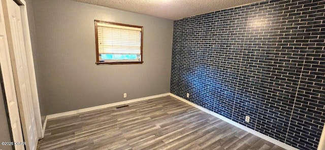 unfurnished bedroom with brick wall, hardwood / wood-style floors, and a textured ceiling