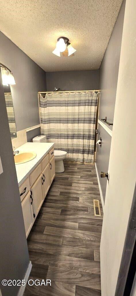 bathroom featuring hardwood / wood-style flooring, vanity, walk in shower, toilet, and a textured ceiling