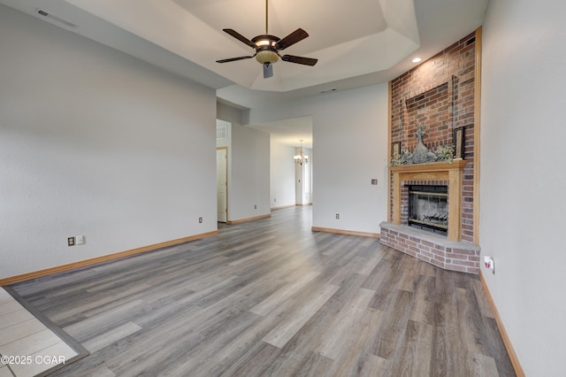 unfurnished living room featuring ceiling fan with notable chandelier, baseboards, a brick fireplace, and wood finished floors