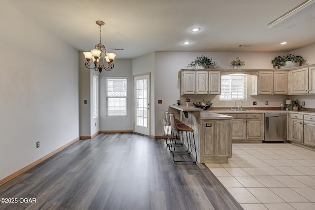 kitchen with an inviting chandelier, a peninsula, light brown cabinets, a kitchen bar, and dishwasher