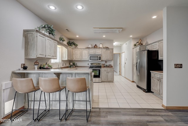 kitchen featuring a peninsula, a kitchen breakfast bar, light countertops, a sink, and appliances with stainless steel finishes