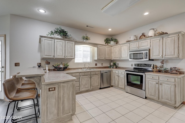 kitchen featuring a kitchen bar, visible vents, appliances with stainless steel finishes, a sink, and a peninsula