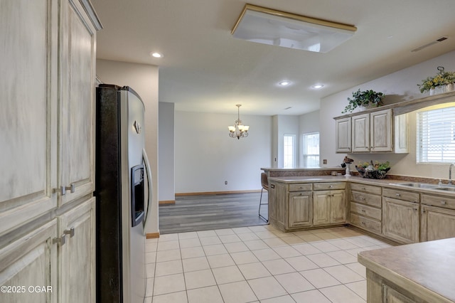 kitchen with light brown cabinetry, stainless steel fridge, a chandelier, a sink, and light tile patterned floors