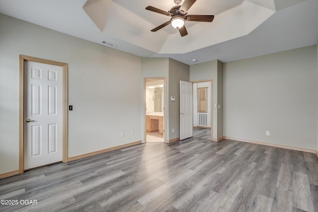 unfurnished bedroom featuring connected bathroom, visible vents, wood finished floors, and a raised ceiling