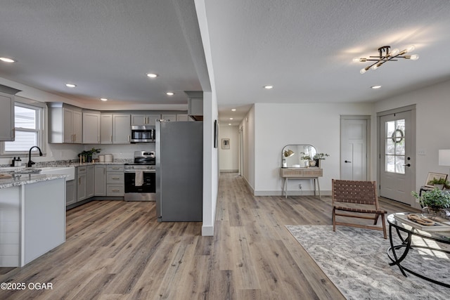 kitchen featuring gray cabinets, stainless steel appliances, light stone countertops, a textured ceiling, and light wood-type flooring