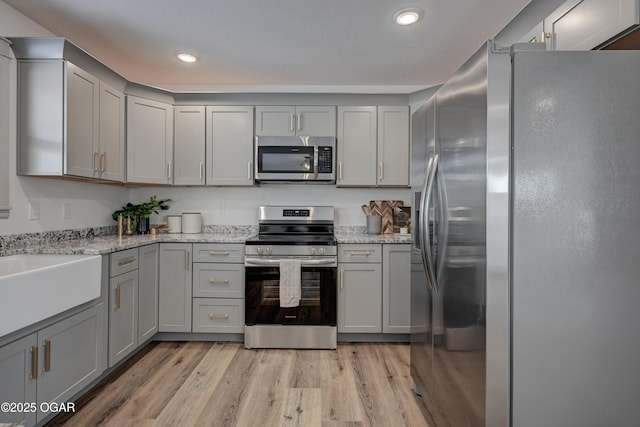 kitchen with sink, gray cabinetry, light stone counters, stainless steel appliances, and light hardwood / wood-style flooring