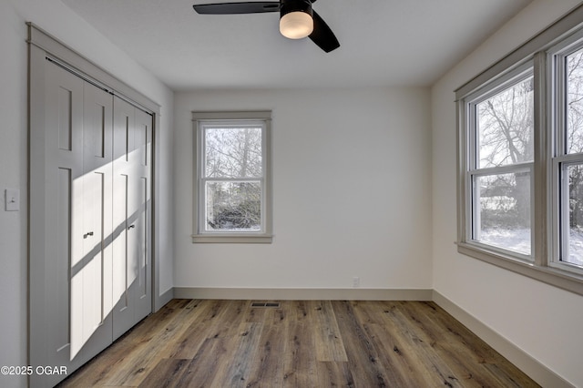 unfurnished bedroom featuring ceiling fan, a closet, hardwood / wood-style floors, and multiple windows