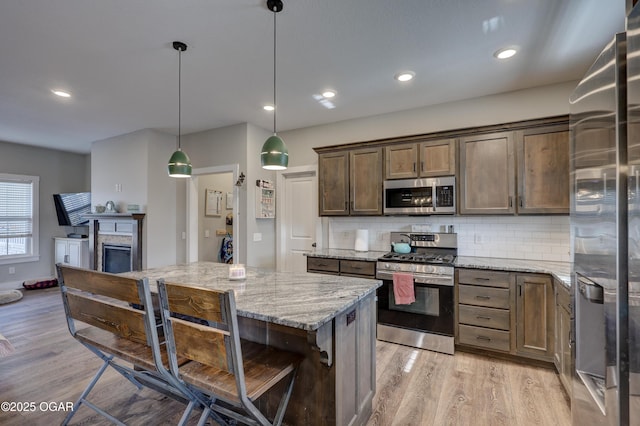 kitchen with light wood-type flooring, stainless steel appliances, a kitchen island, light stone counters, and pendant lighting