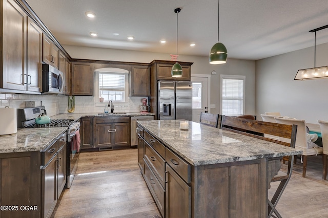 kitchen with hanging light fixtures, a center island, sink, light stone counters, and appliances with stainless steel finishes