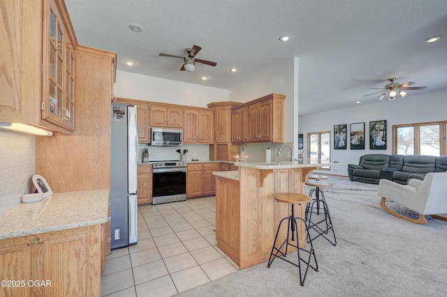 kitchen featuring light tile patterned floors, a breakfast bar, appliances with stainless steel finishes, a healthy amount of sunlight, and kitchen peninsula