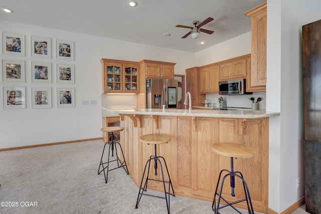 kitchen with light colored carpet, stainless steel appliances, a kitchen breakfast bar, and kitchen peninsula