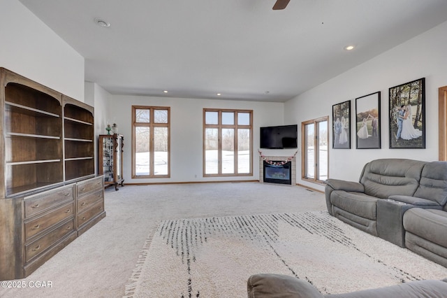 living area featuring a glass covered fireplace, light carpet, baseboards, and recessed lighting