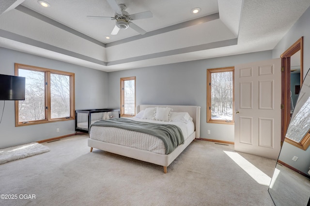 bedroom featuring light colored carpet, a textured ceiling, ceiling fan, and a tray ceiling