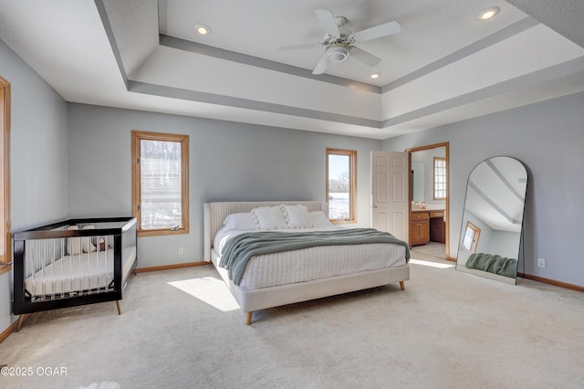 carpeted bedroom with ceiling fan, ensuite bath, and a tray ceiling