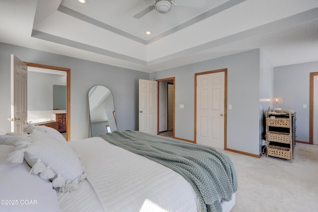 carpeted bedroom with ensuite bathroom, ceiling fan, and a tray ceiling