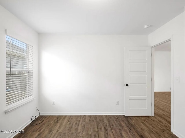 spare room with baseboards and dark wood-type flooring