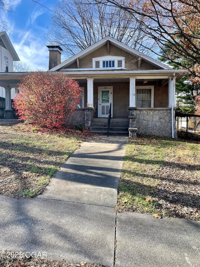 view of front of house featuring stone siding, a porch, and a chimney