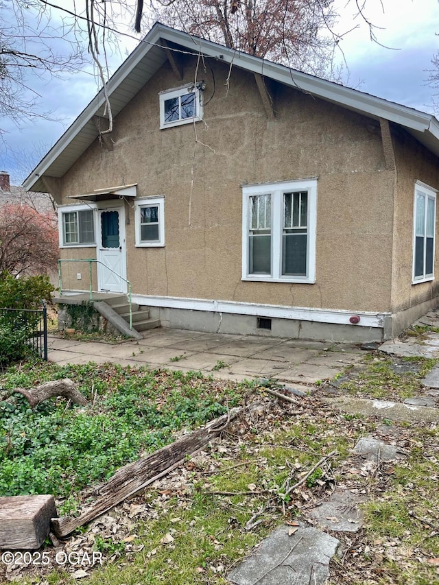 rear view of property with entry steps, crawl space, and stucco siding