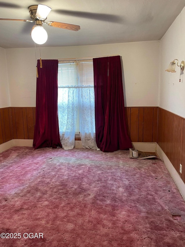 unfurnished room with ceiling fan, wooden walls, carpet floors, and wainscoting