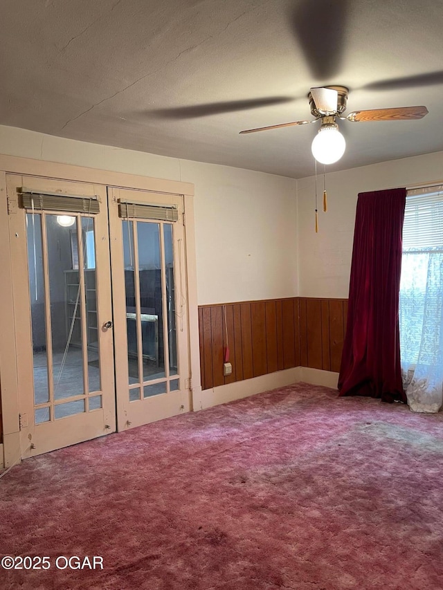 carpeted spare room with wainscoting, ceiling fan, french doors, wood walls, and a textured ceiling