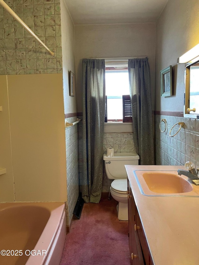 full bath with a wainscoted wall, toilet, vanity, a bathtub, and tile walls