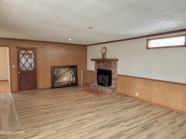 unfurnished living room with crown molding, a brick fireplace, a textured ceiling, and light wood-type flooring