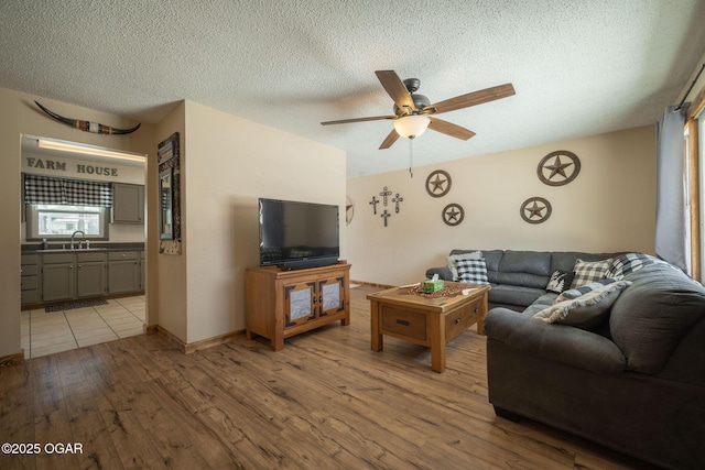 living room featuring ceiling fan, sink, a textured ceiling, and light hardwood / wood-style flooring