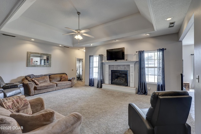 living room featuring a fireplace, carpet flooring, ceiling fan, and a raised ceiling