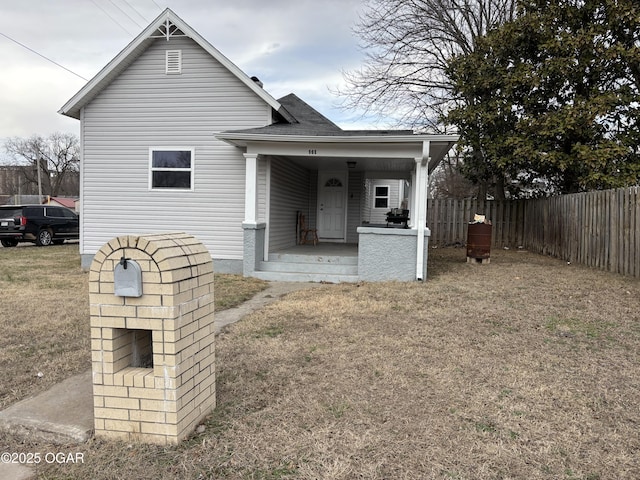 back of house with roof with shingles, a porch, a lawn, and fence