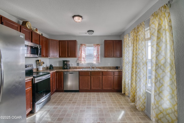 kitchen with appliances with stainless steel finishes, brown cabinets, light countertops, a textured ceiling, and a sink