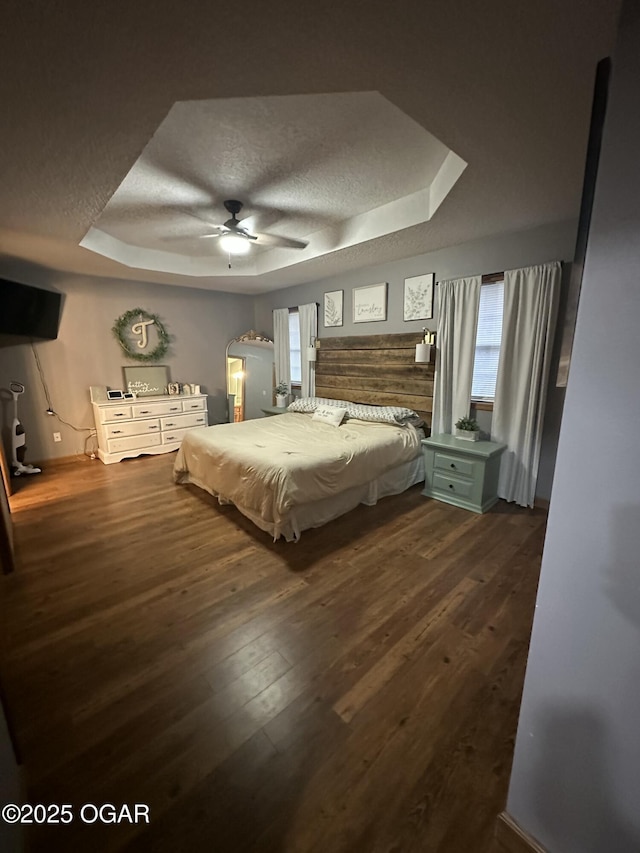 bedroom with dark wood-type flooring, a raised ceiling, ceiling fan, and a textured ceiling