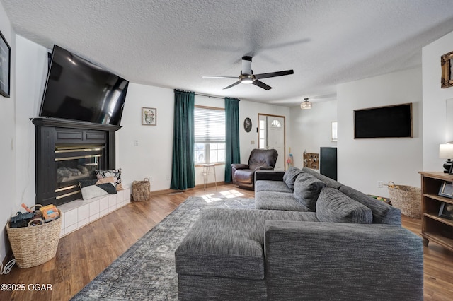 living area featuring a textured ceiling, ceiling fan, a tile fireplace, and wood finished floors