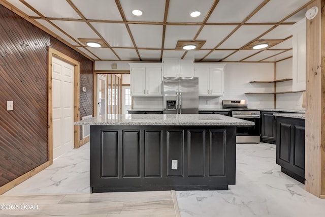 kitchen featuring marble finish floor, appliances with stainless steel finishes, white cabinets, a kitchen island, and wood walls