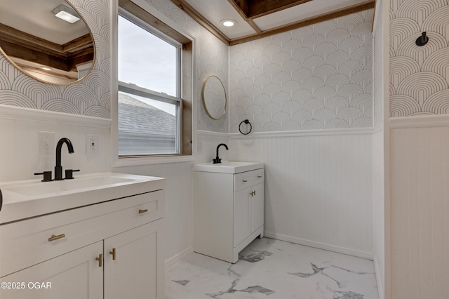 bathroom with wallpapered walls, wainscoting, a sink, marble finish floor, and two vanities