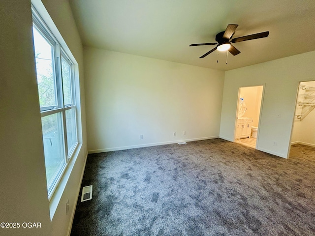 unfurnished bedroom with visible vents, a walk in closet, and dark colored carpet