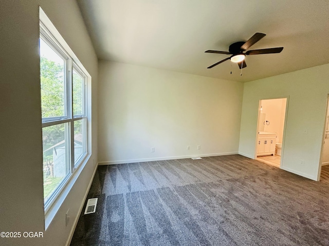 carpeted spare room featuring baseboards, ceiling fan, visible vents, and plenty of natural light