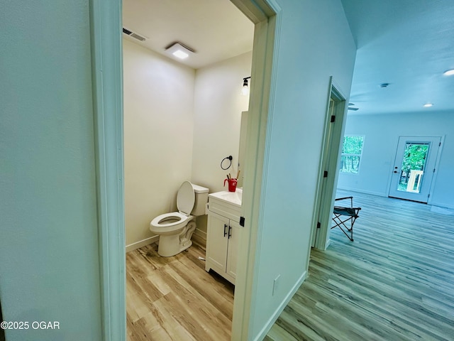 half bath featuring toilet, baseboards, visible vents, vanity, and wood finished floors
