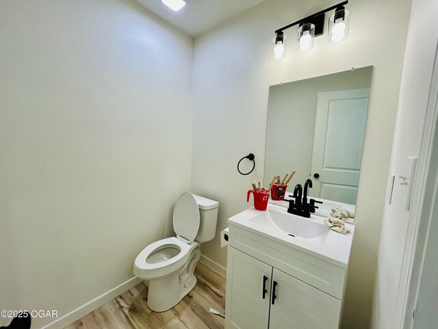 half bathroom with vanity, toilet, baseboards, and wood finished floors