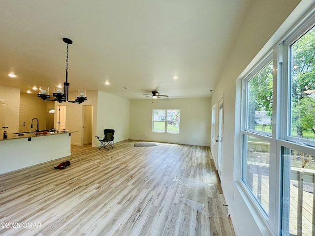 unfurnished living room featuring light wood-style floors, baseboards, ceiling fan with notable chandelier, and recessed lighting