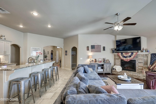 living area featuring arched walkways, a fireplace, lofted ceiling, visible vents, and a ceiling fan