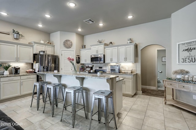 kitchen featuring visible vents, light stone counters, appliances with stainless steel finishes, and a center island with sink