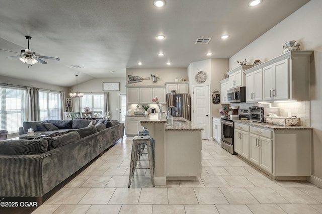 kitchen with a center island with sink, light stone counters, open floor plan, stainless steel appliances, and white cabinetry