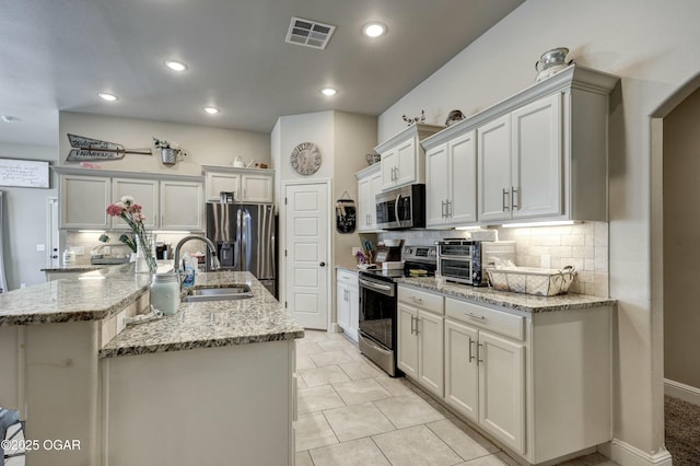 kitchen featuring stainless steel appliances, visible vents, light stone counters, and a spacious island