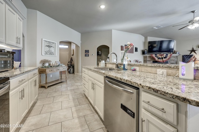 kitchen with arched walkways, light stone counters, a sink, white cabinetry, and dishwasher