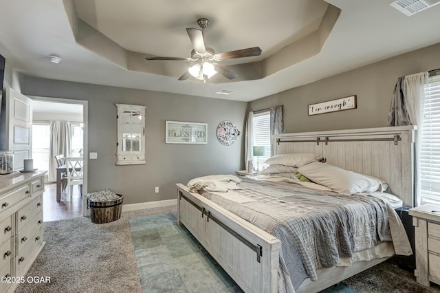 bedroom featuring baseboards, multiple windows, visible vents, and a raised ceiling