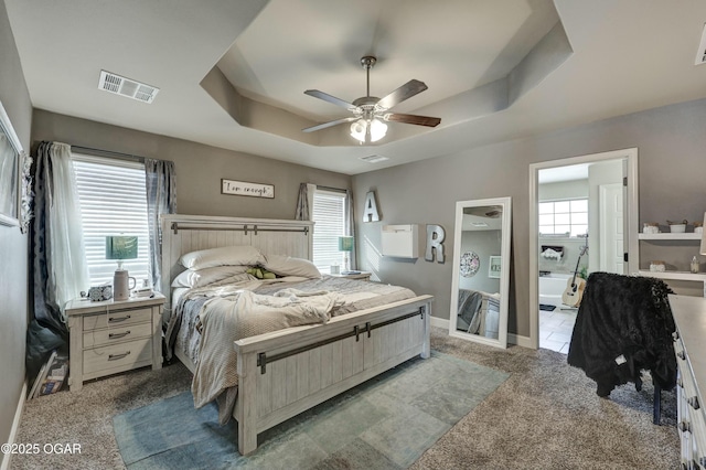 bedroom featuring baseboards, visible vents, a ceiling fan, light colored carpet, and a tray ceiling