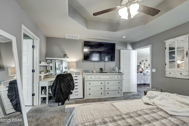 carpeted bedroom with a ceiling fan, a tray ceiling, and visible vents